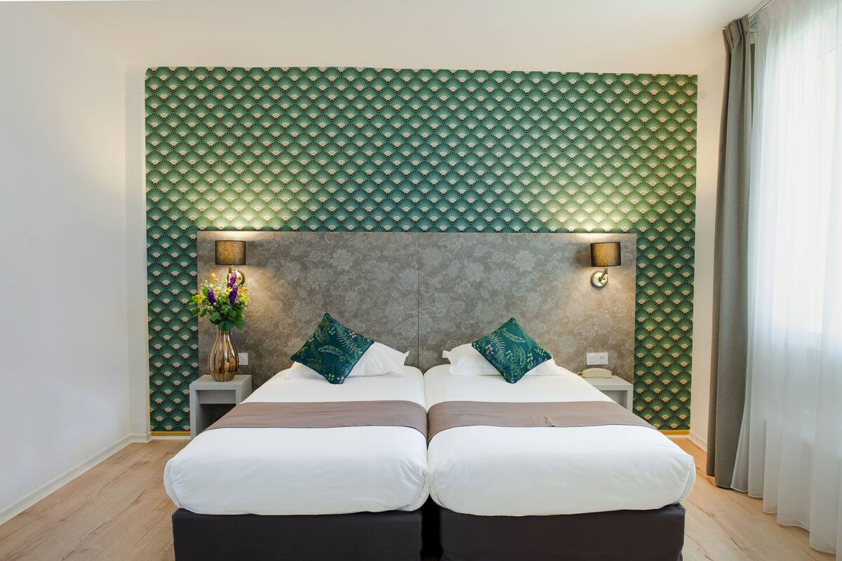 A double bed with a headboard, bedside tables, and a vase with flowers.