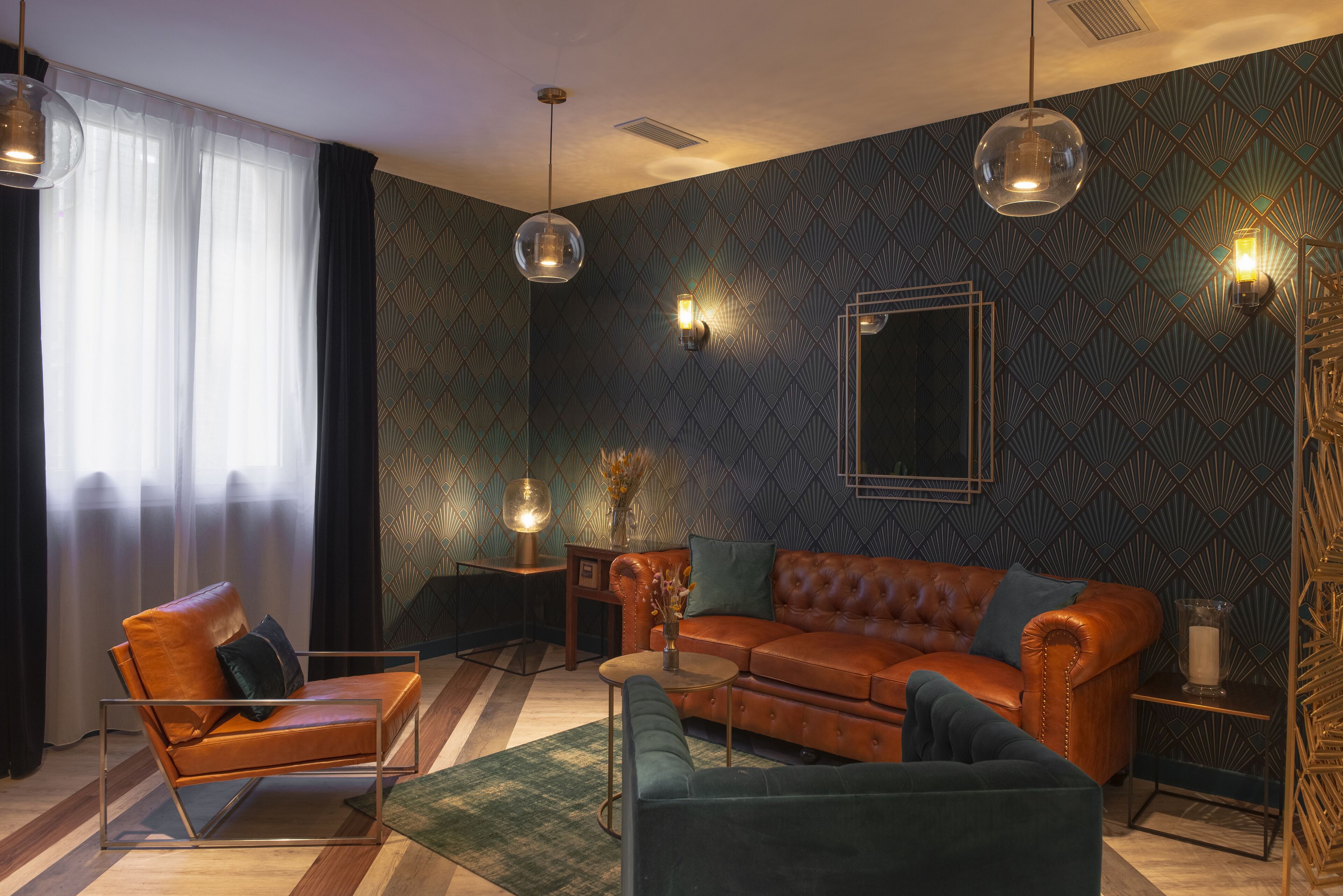 A modern living room with a leather sofa, a green armchair, and a coffee table. There are two pendant lights and a wall-mounted light fixture.
