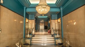 Een statige lobby met een grote kroonluchter, marmeren trappen en moderne zitplaatsen.