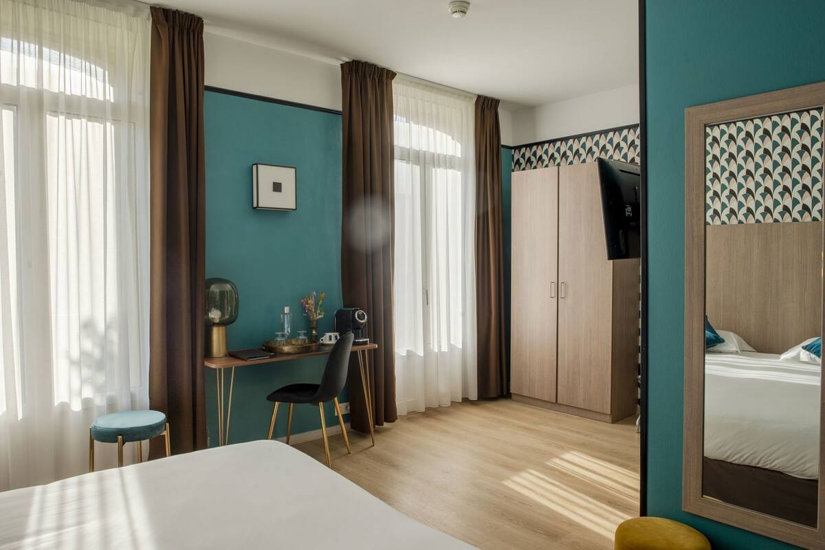 A hotel room with a bed, a desk with a chair, a TV, and a wardrobe.