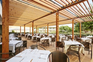 Dine al fresco under a shaded pergola with tables set for a meal.