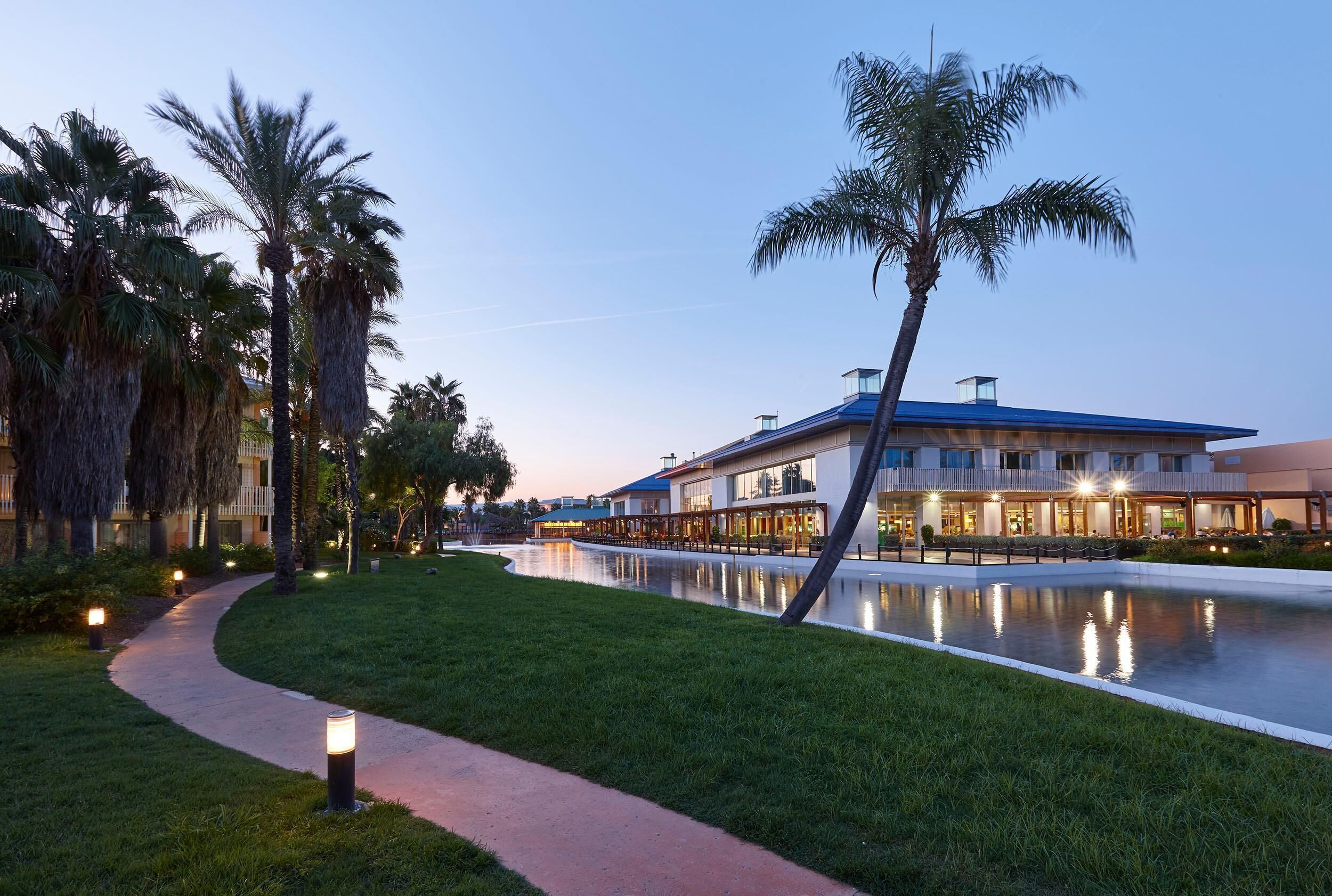 A hotel with a pool, palm trees, and a pathway.