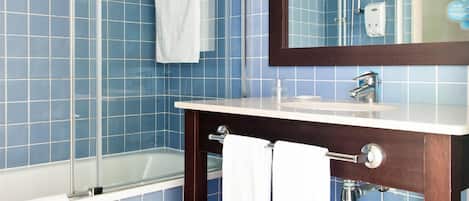 A bathroom with blue tiled walls, a glass shower enclosure, a wooden vanity with a mirror, and a white towel hanging on the wall.