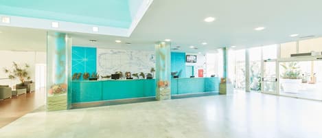 A spacious lobby with a reception desk, large windows, and a high ceiling.