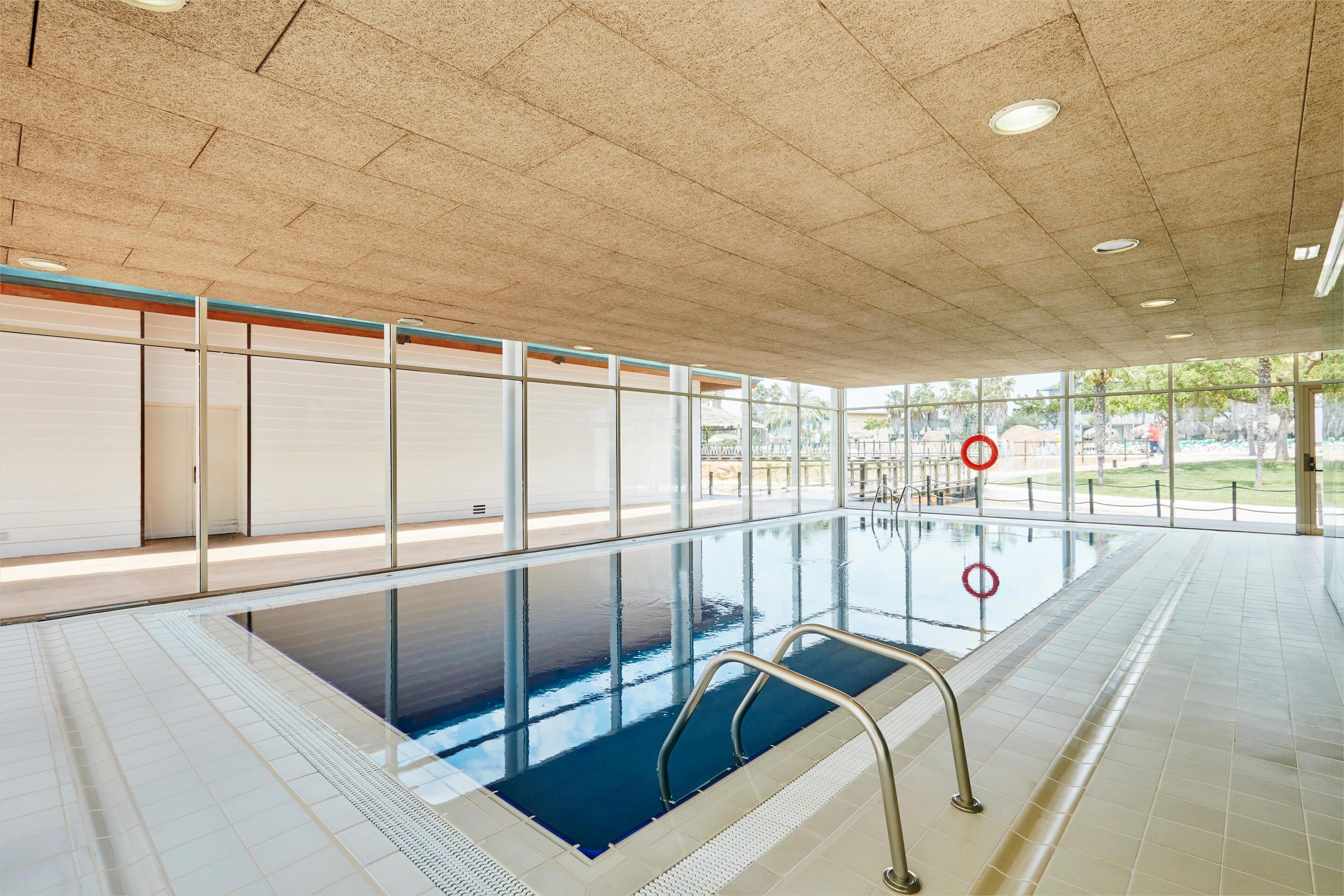 Una piscina interior con paredes de vidrio transparente, suelo de baldosas y barandillas metálicas.