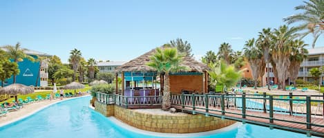 A swimming pool with lounge chairs and a small bar area surrounded by palm trees.