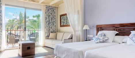 A bedroom with two beds, a wooden headboard, a nightstand, a ceiling fan, a balcony with a view of palm trees, and a sliding glass door with curtains.