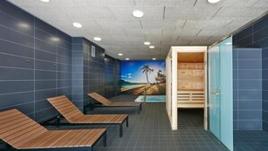 A sauna room with wooden benches, a mural of a beach, and a wooden sauna cabin.