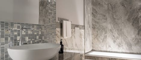 Une salle de bain moderne avec un grand lavabo sur pied, une douche à l’italienne en verre et des murs en marbre.