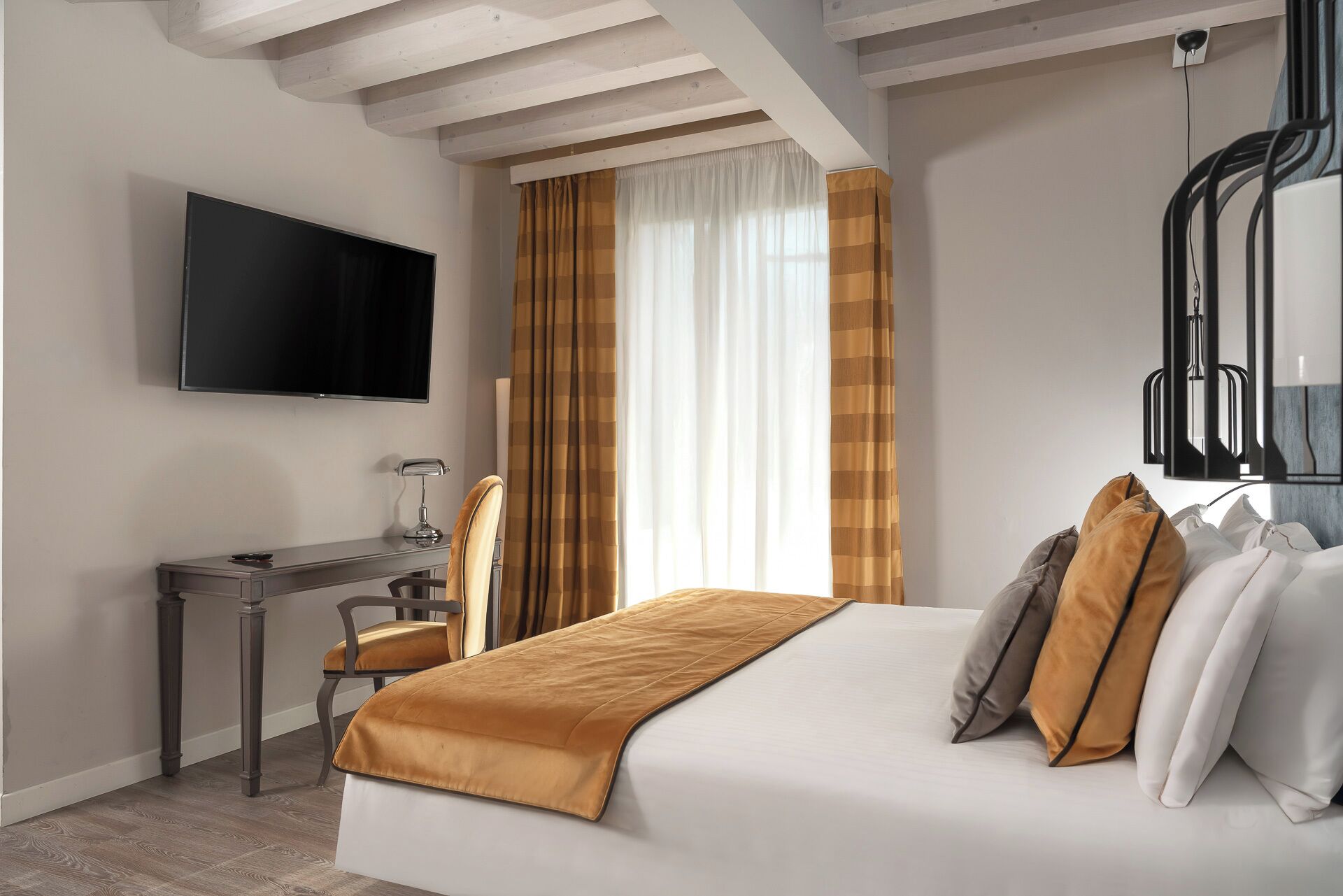 Een hotelkamer met een bed, een bureau met stoel, een aan de muur bevestigde televisie en een raam met gordijnen.