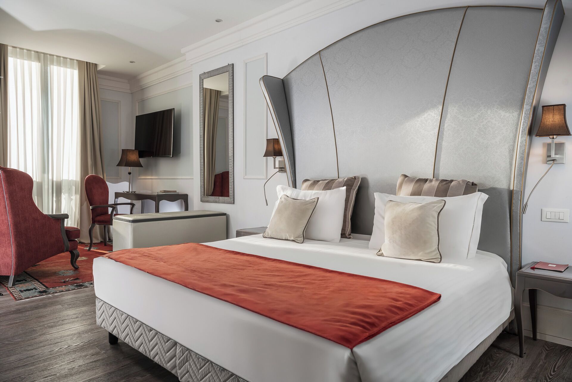 Une chambre d’hôtel avec un grand lit, un bureau, une télévision et un fauteuil rouge.