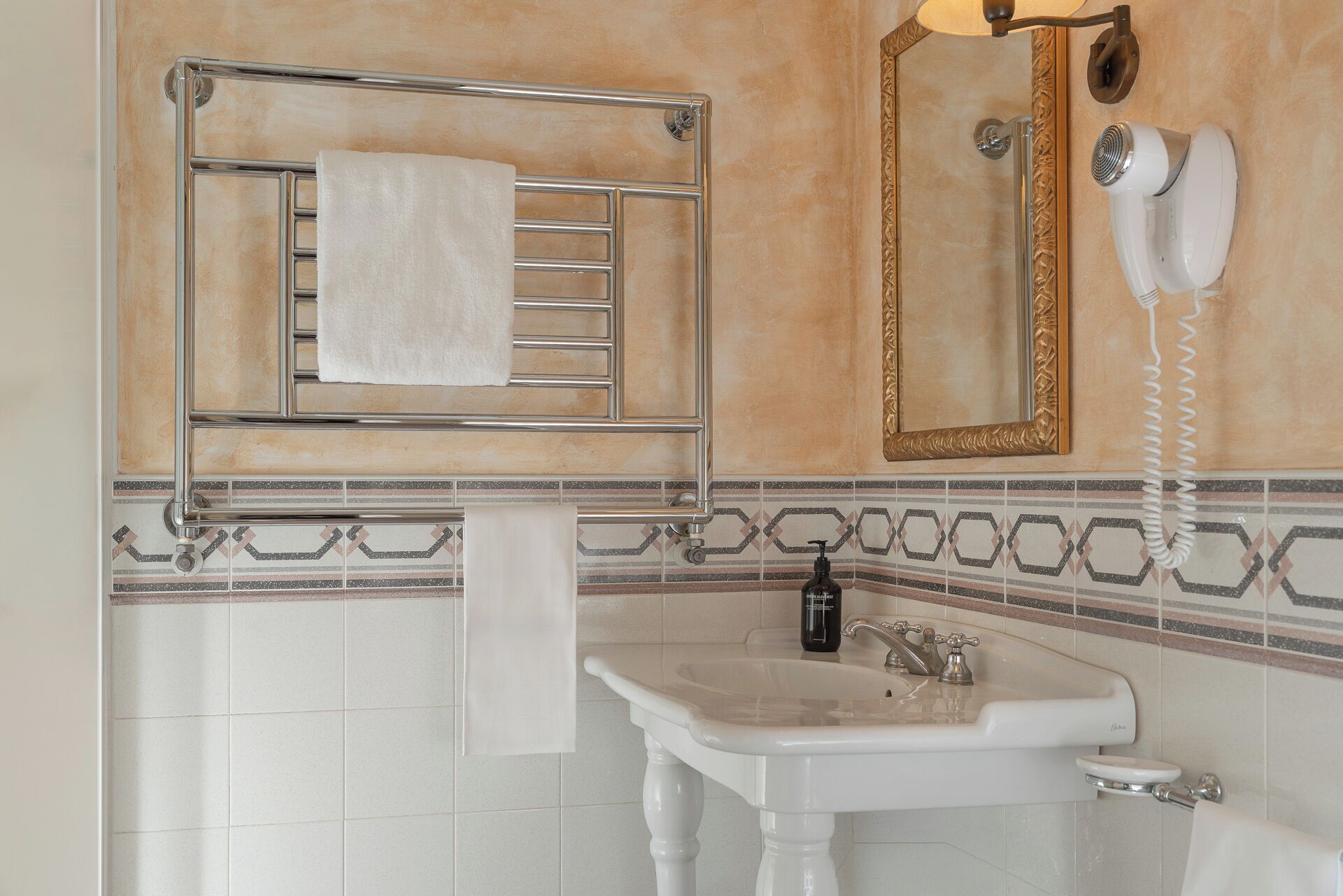 A bathroom with a white sink, a towel rack with a white towel, a mirror with a gold frame, and a hairdryer.