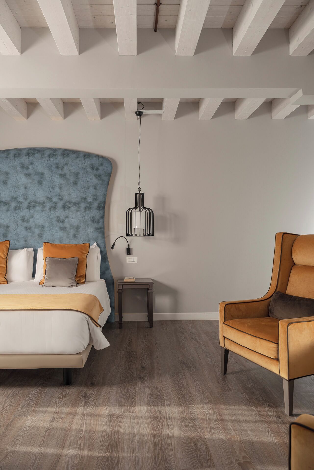 A modern bedroom with a large bed, a side table, a chair, and a hanging light fixture.