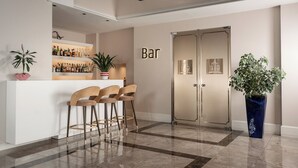 Zona de bar con mostrador, taburetes y una estantería llena de botellas.