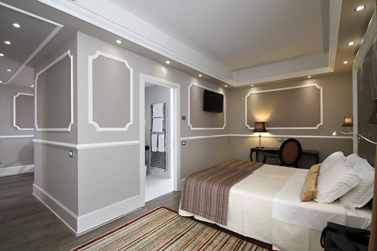 A modern hotel room with a large bed, a flat-screen TV, and a small desk with a lamp.
