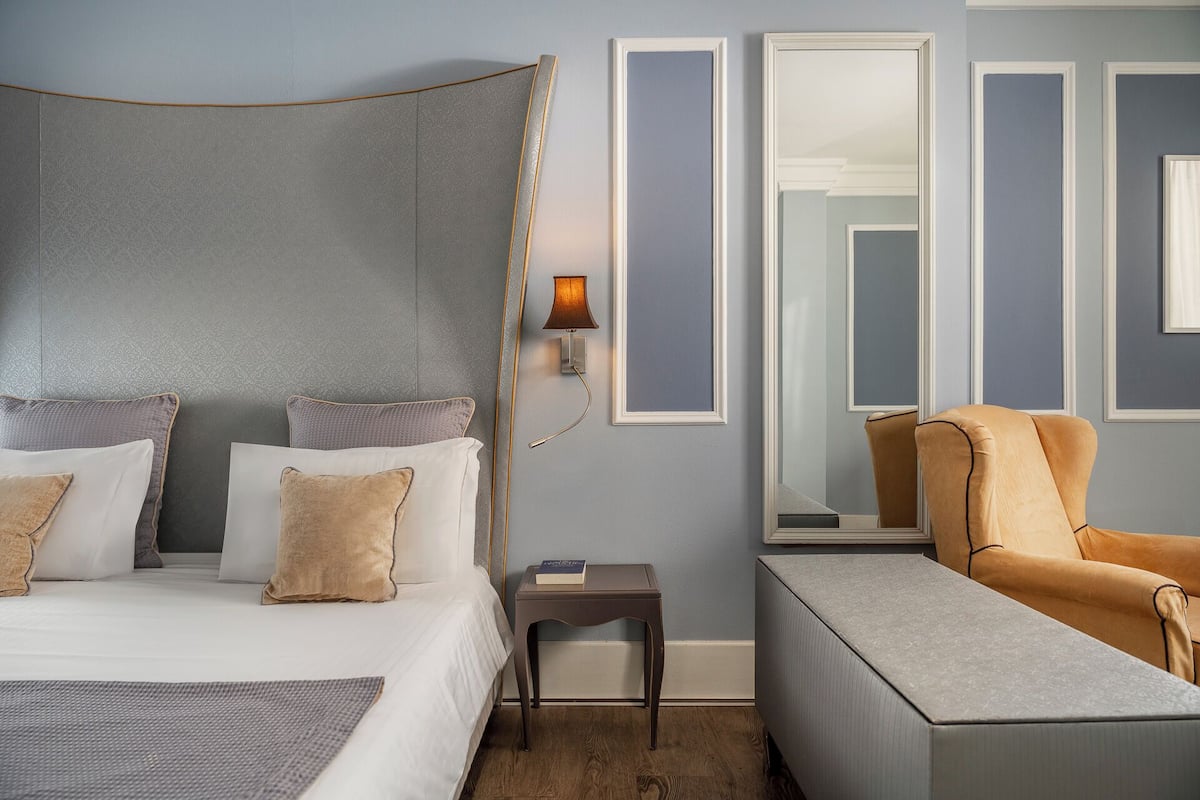 A hotel room with a bed, a nightstand, a reading lamp, a chair, and a large mirror.