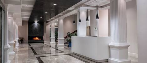 A modern lobby with a marble floor, a reception desk, and a fireplace.