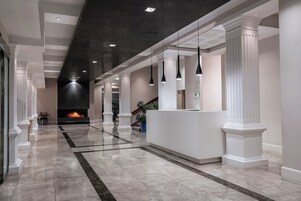 A modern lobby with a marble floor, a reception desk, and a fireplace.
