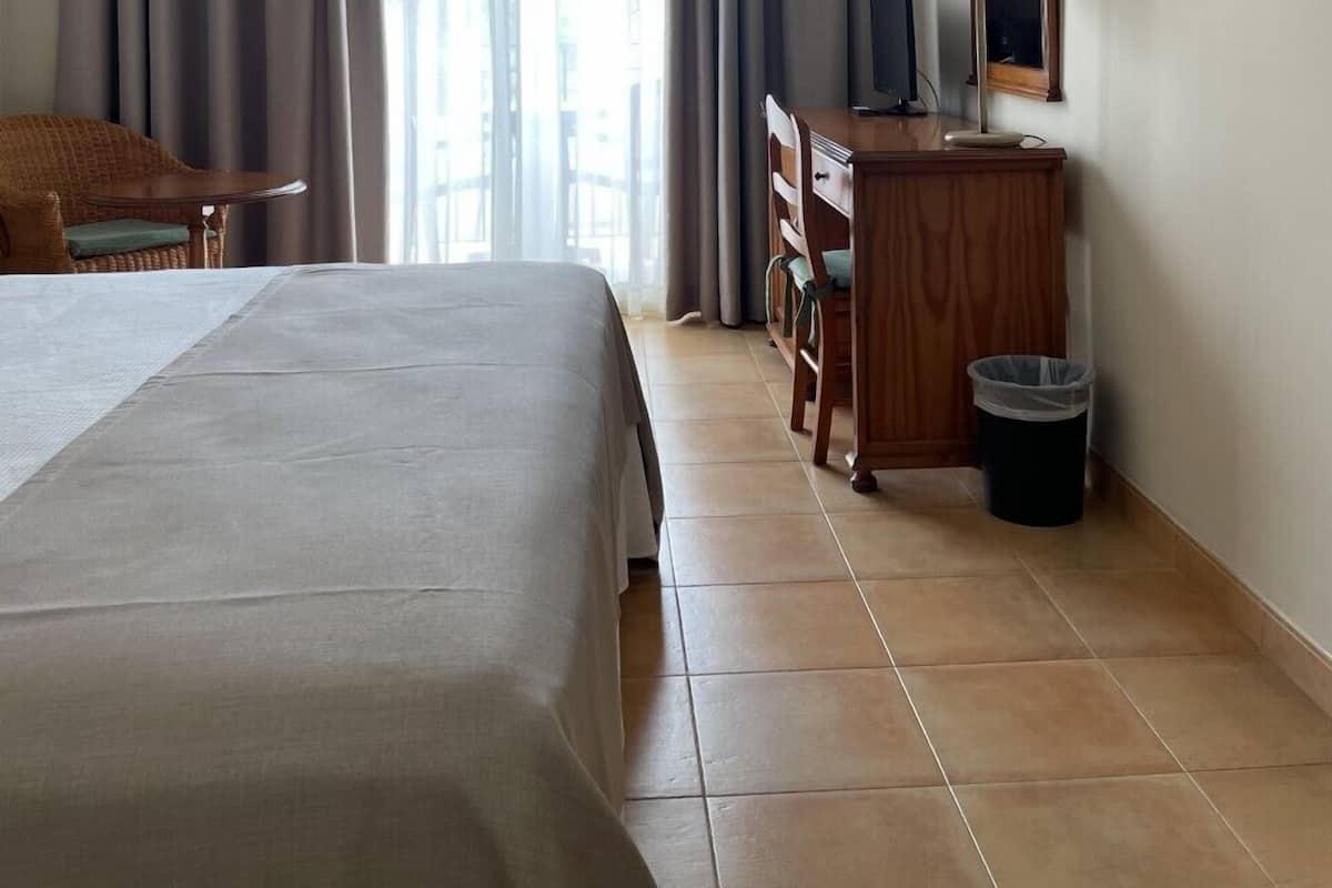 A hotel room with a large bed, a desk with a lamp, a chair, and a trash bin.