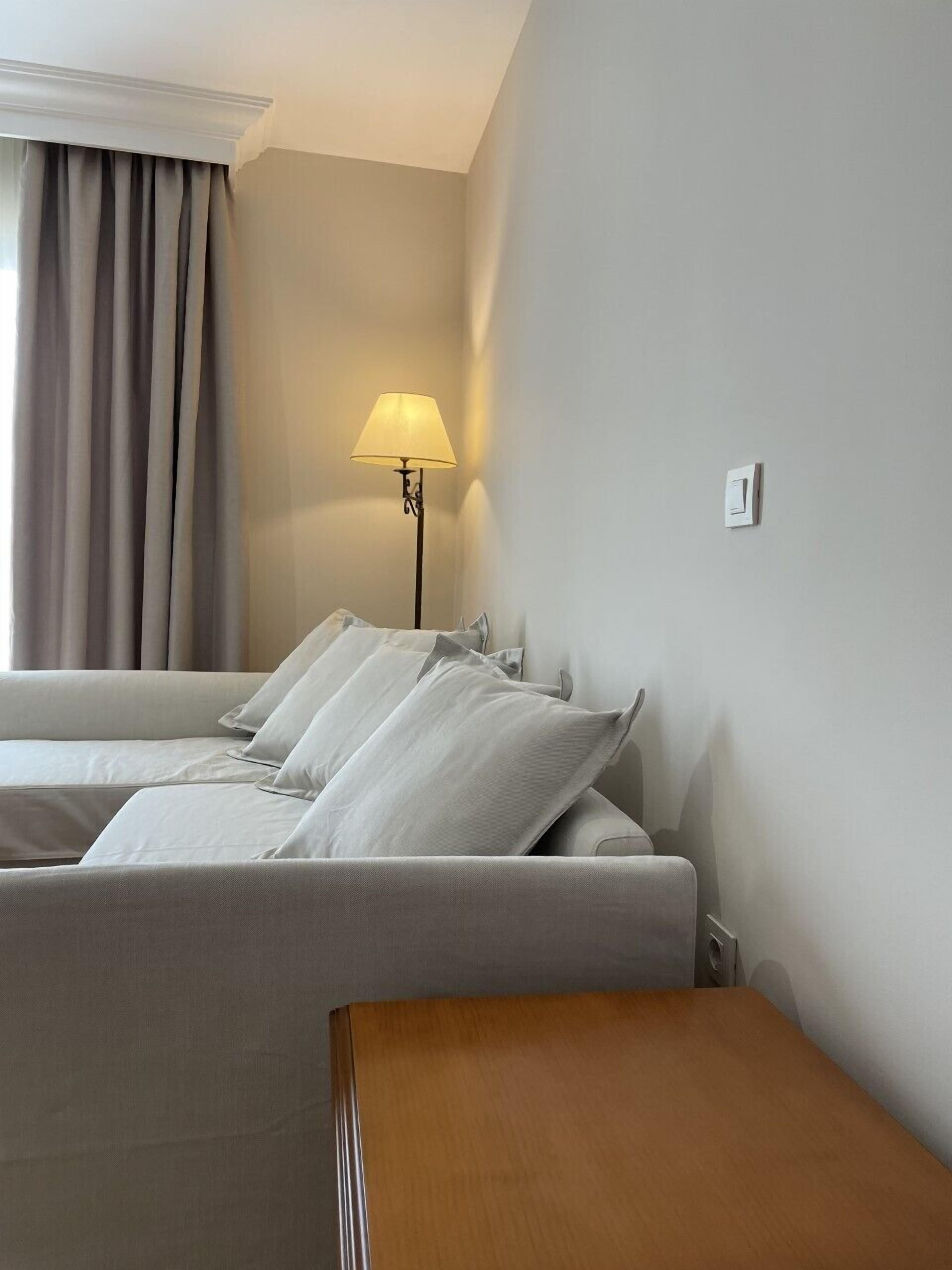 A hotel room with a bed, a bedside table, a lamp, and a window with curtains.