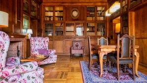 A library with wooden bookshelves, a large clock, and a chessboard on a table. - Els Jardins De La Martana (Besalu)
