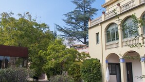 A building with a balcony, arched windows, and a garden with trees and shrubs. - Els Jardins De La Martana (Besalu)