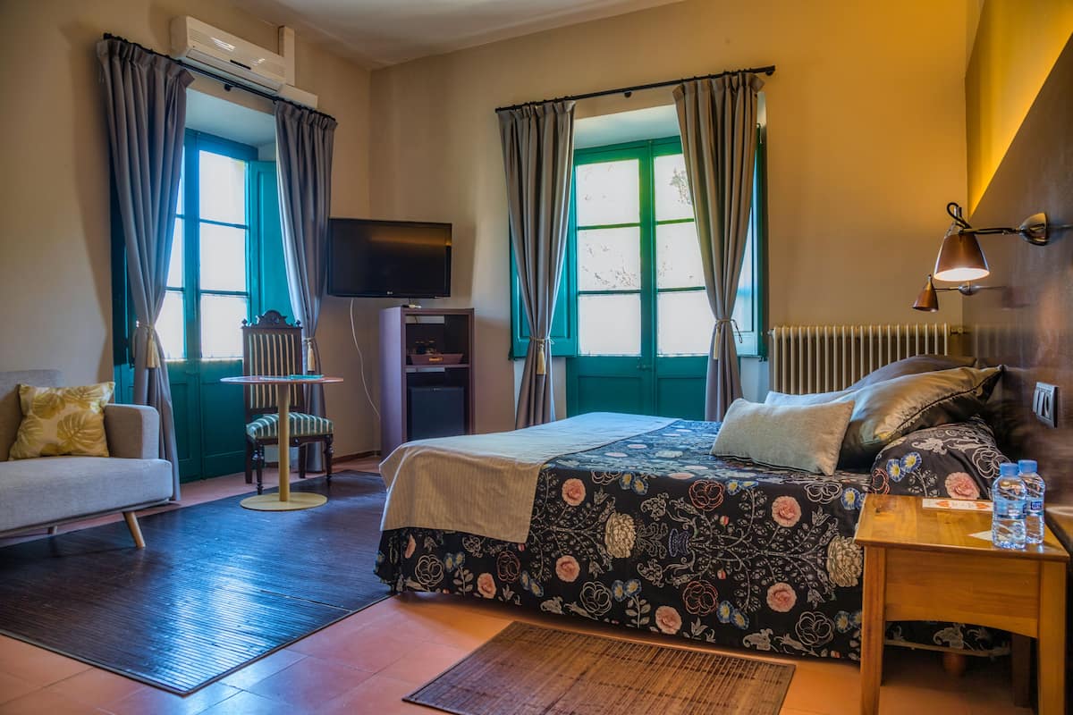 A hotel room with a bed, a sofa, a TV, a table with water bottles, and a radiator.