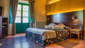 A bedroom with a bed, a bedside table, a lamp, a radiator, and a window with curtains. - Els Jardins De La Martana (Besalu)