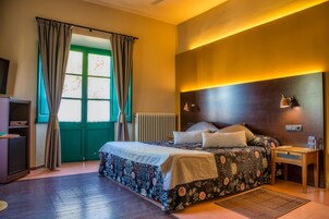 Un dormitorio con cama, mesita de noche, lámpara, radiador y ventana con cortinas.