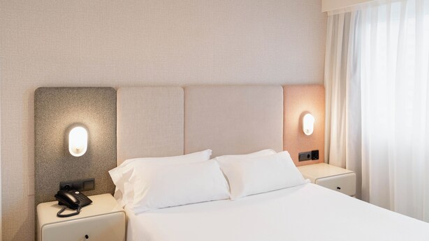Ein Hotelzimmer mit einem Bett, zwei Nachttischen, einem Telefon und Wandleuchten.