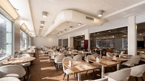 Un restaurante espacioso con varias mesas y sillas, ventanas amplias y un diseño moderno de techo.