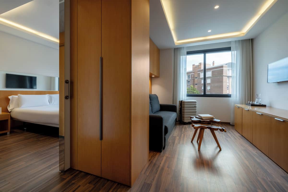 Ein modernes Hotelzimmer mit Bett, einer Sitzecke, einem Schreibtisch und einem großen Fenster mit Blick auf die Stadt.