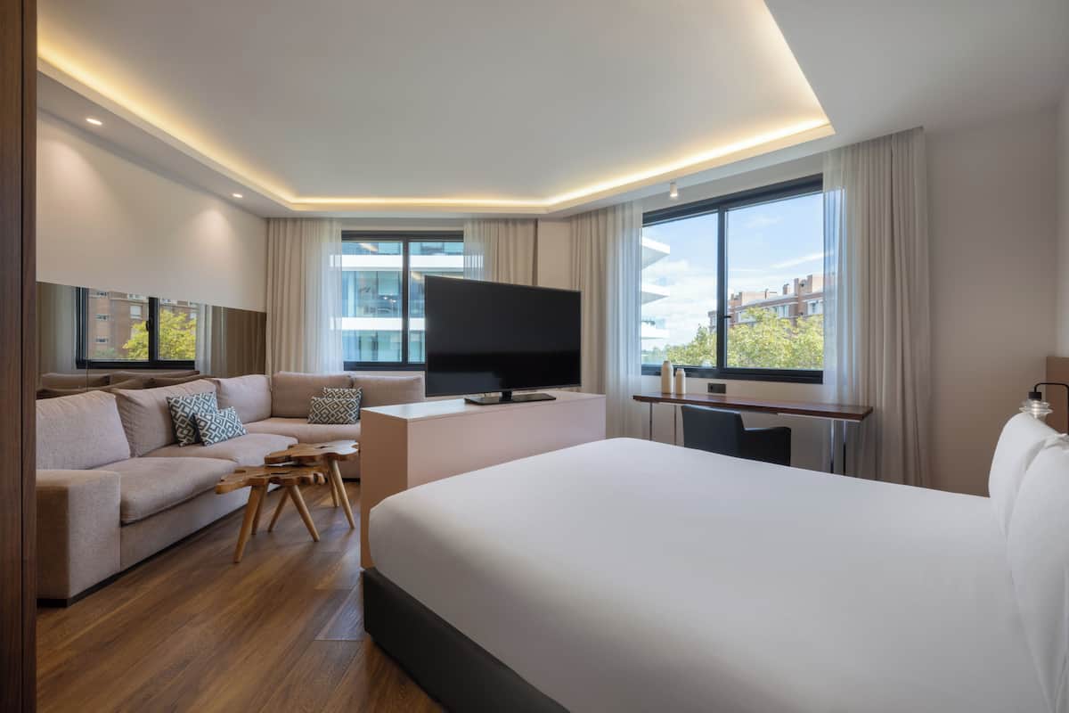 Ein modernes Hotelzimmer mit einem großen Bett, einer Couch, einem Fernseher und einem Schreibtisch.