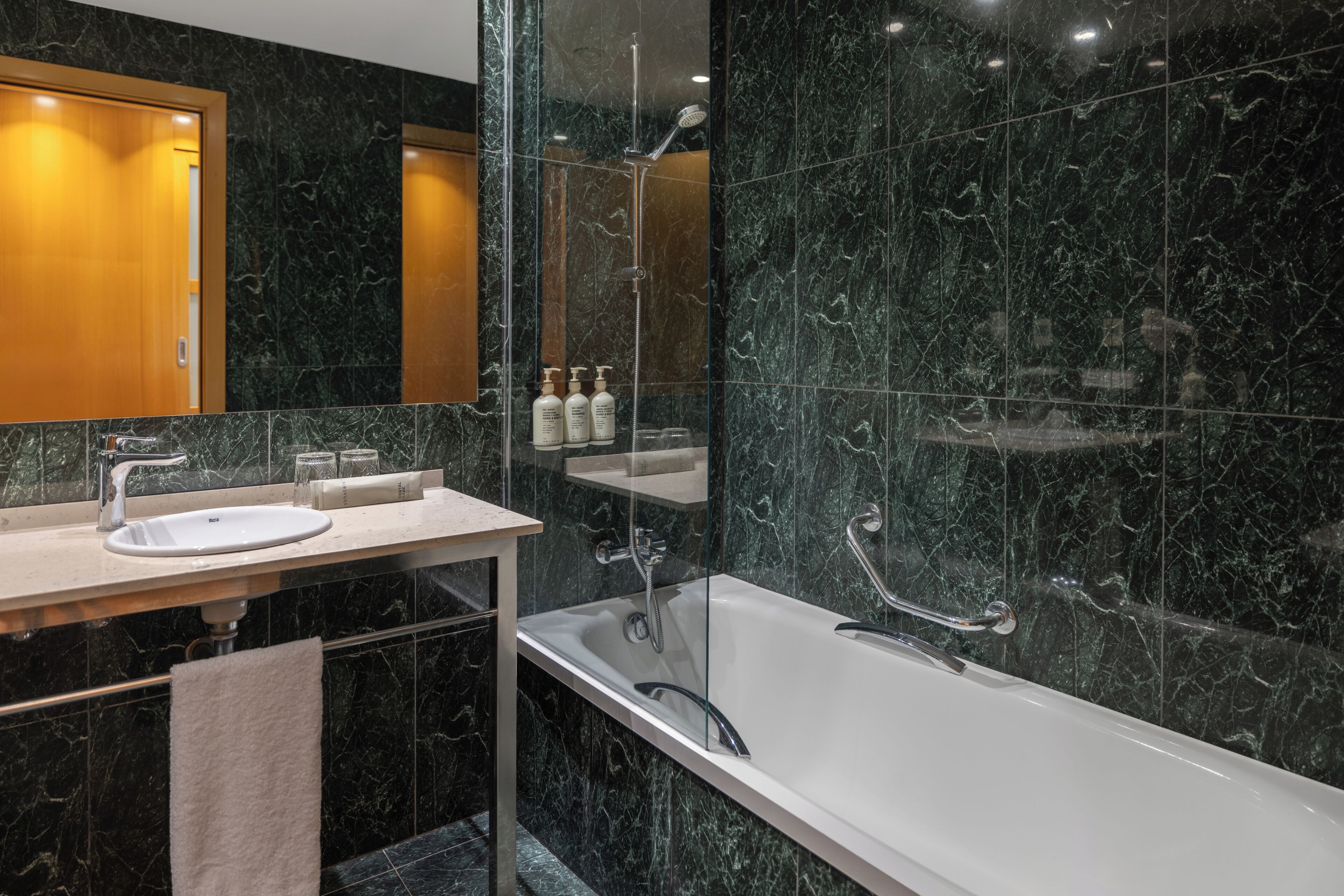 Un baño moderno con lavamanos de mármol, bañera y ducha con mampara de vidrio.
