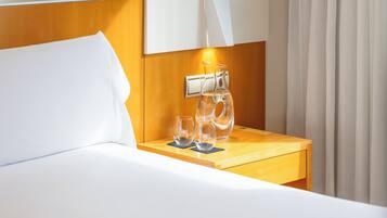 Een hotelkamer met een bed, een nachtkastje met een lamp en een raam met gordijnen.