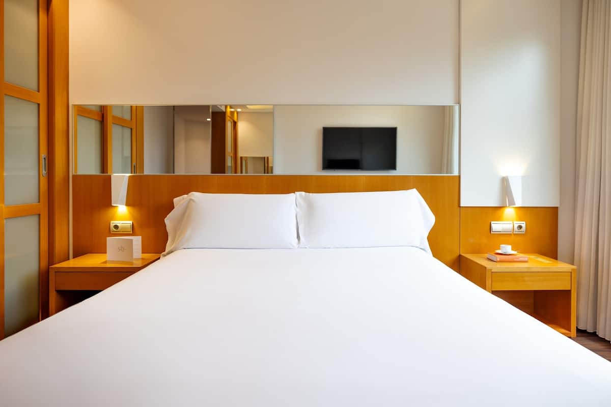 Ein Hotelzimmer mit einem großen Bett, einem Holz-Kopfteil, Nachttischen mit Lampen, einem Flachbildfernseher und einem Spiegel.