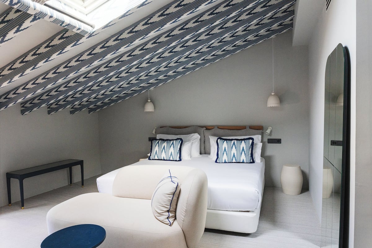 Een moderne slaapkamer met een bed, nachtkastjes, een bankje en een dakraam.