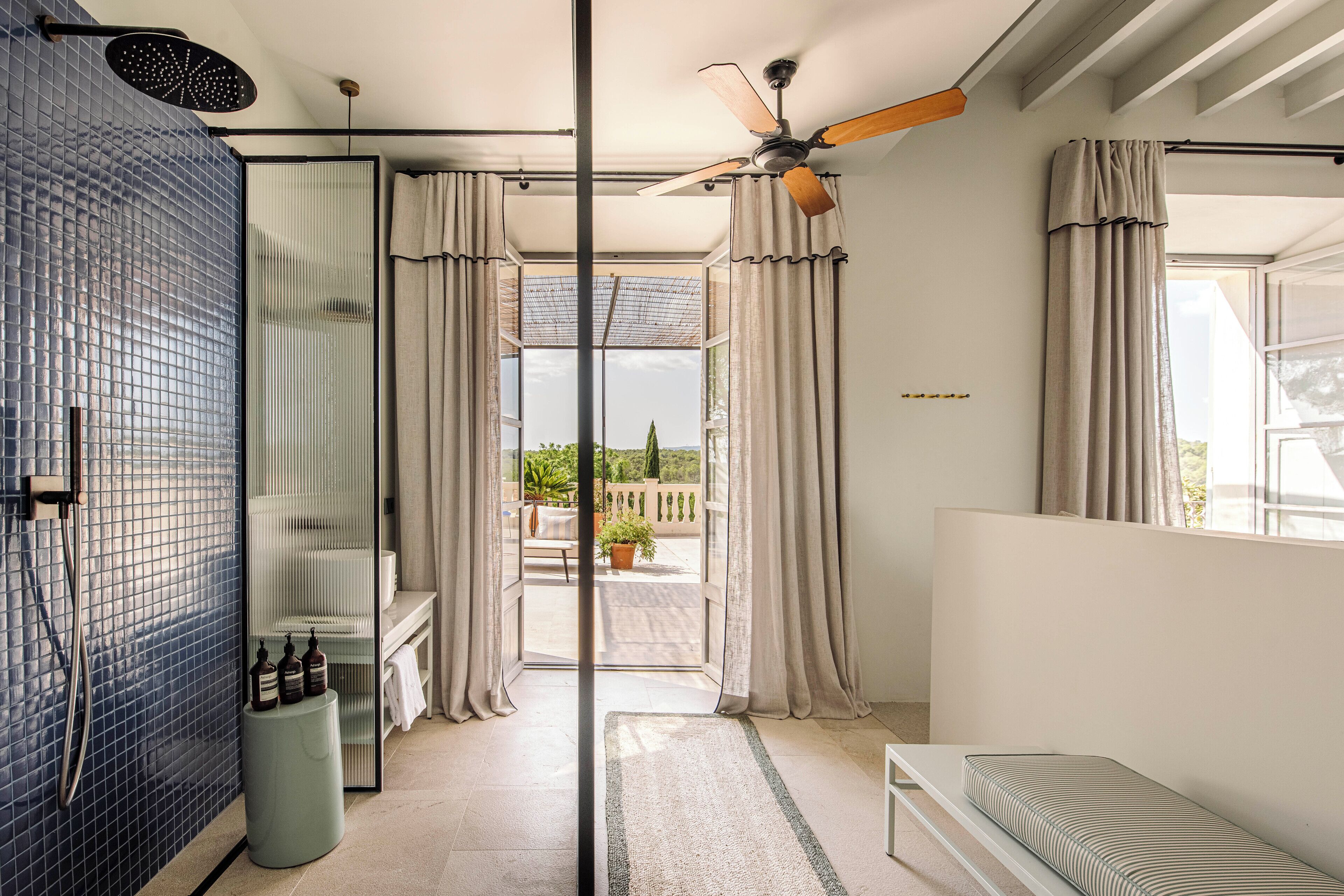 A modern bathroom with a glass shower enclosure, a ceiling fan, and a view of the outdoors.