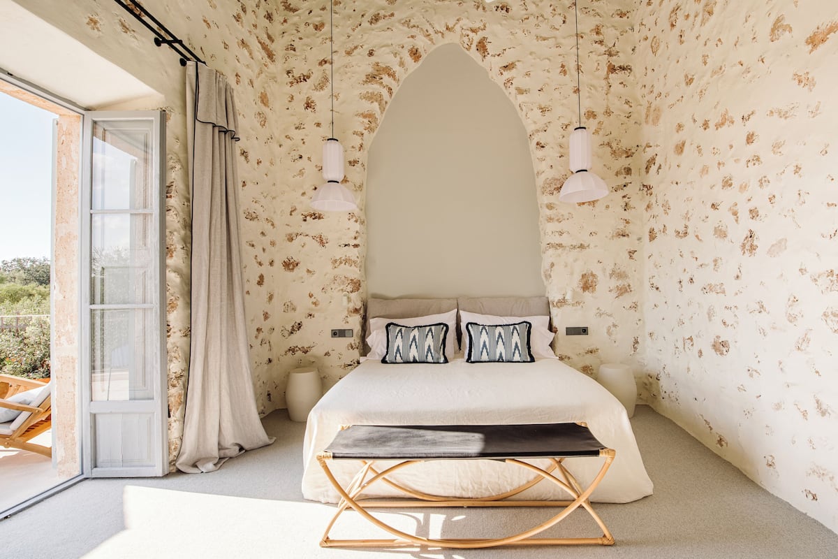 Een slaapkamer met een groot bed, twee hanglampen, een houten bankje en uitzicht door een glazen deur.