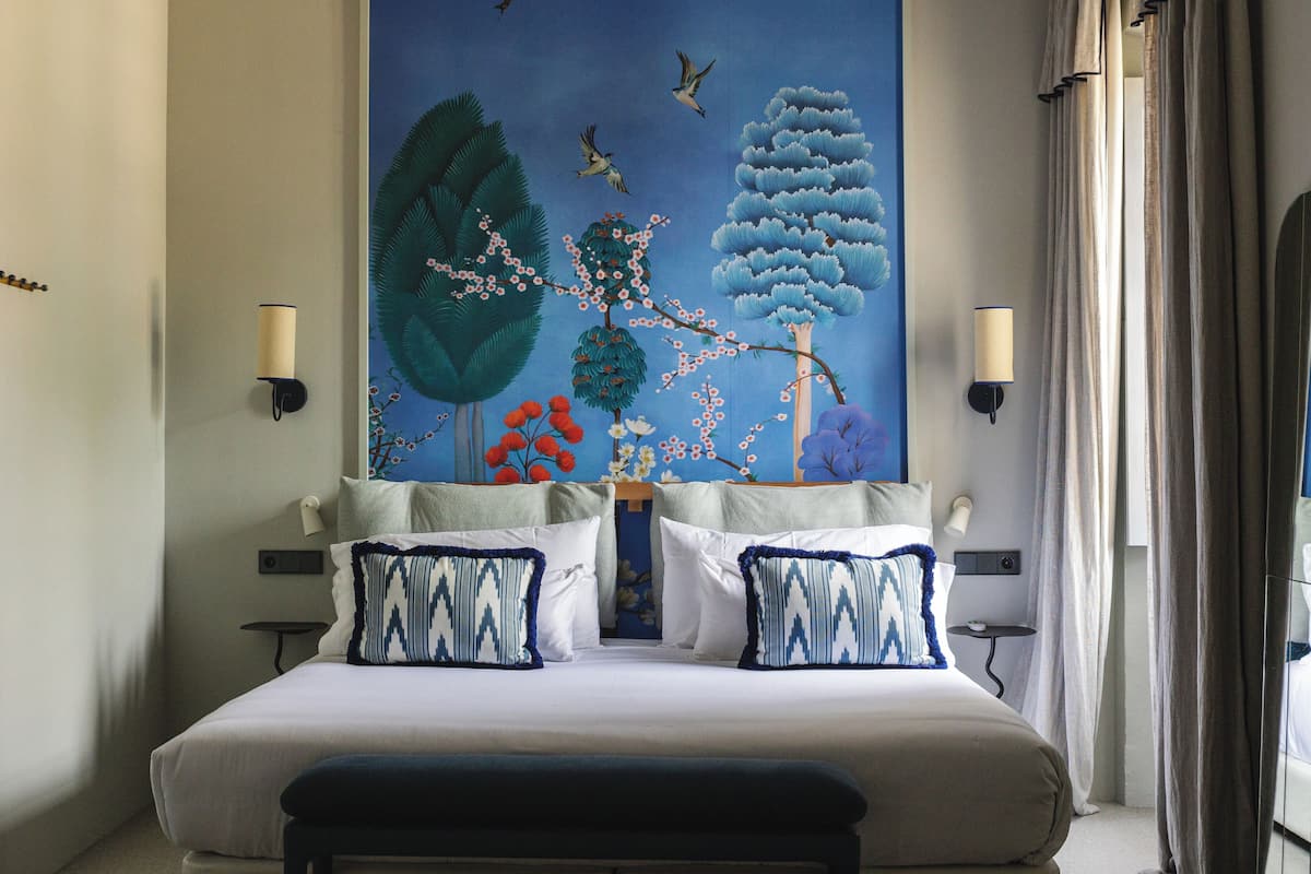 Een slaapkamer met een groot bed, twee nachtkastjes en een muurschildering.