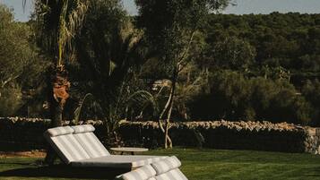 Dos sillones de relax con cojines a rayas sobre un césped, una pequeña mesa redonda y un muro de piedra al fondo.