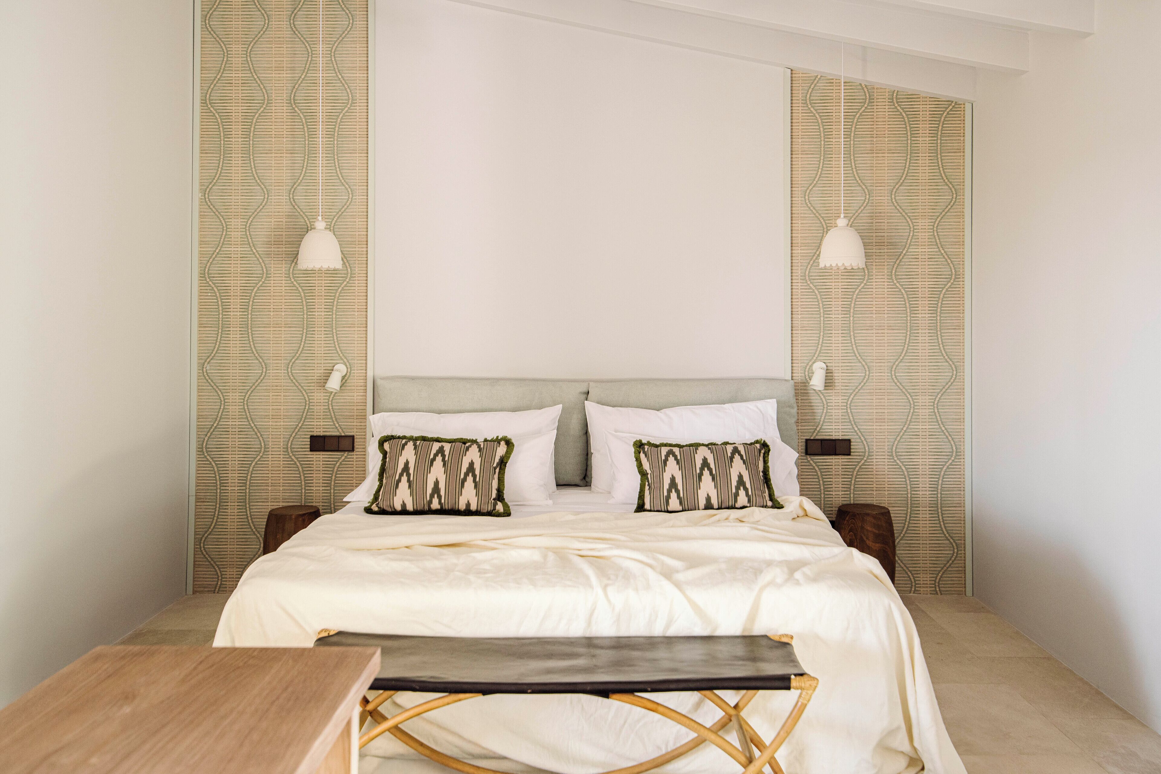 Un dormitorio ordenado con cama, mesitas de noche y lámparas colgantes.