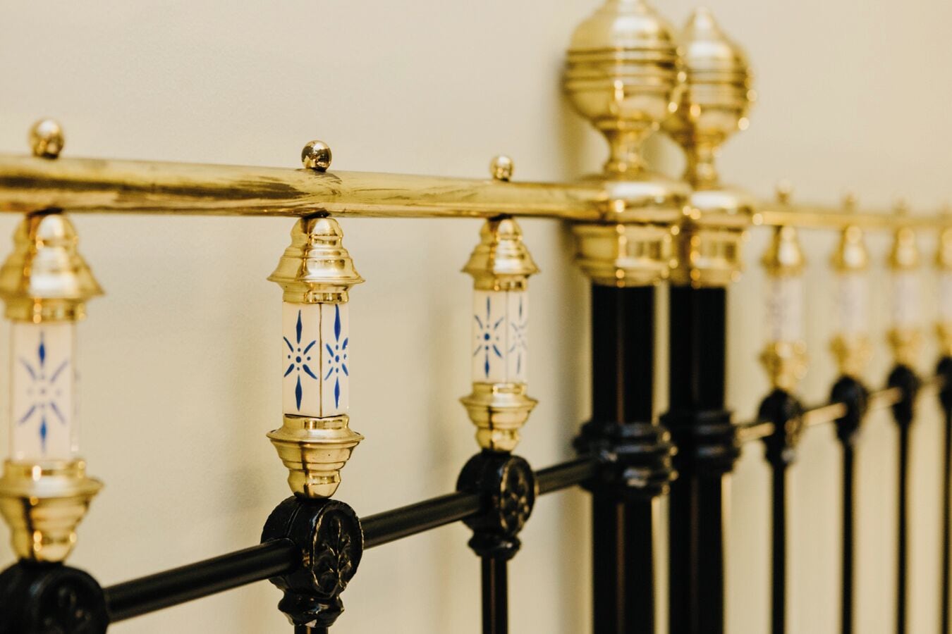 Un gros plan d’une rambarde en métal noir ornée de balustres de couleur or et d’éléments en céramique blanche aux motifs bleus.