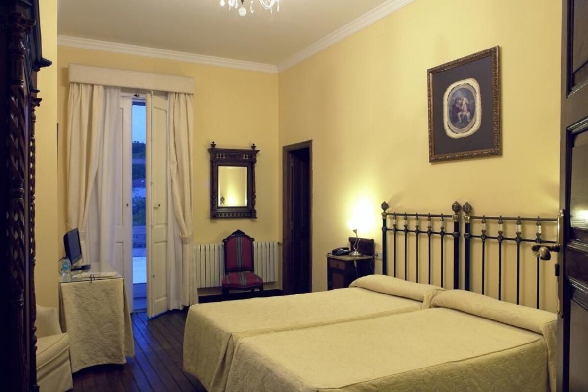 A hotel room with two beds, a desk with a computer, a chair, a mirror, and a picture on the wall.