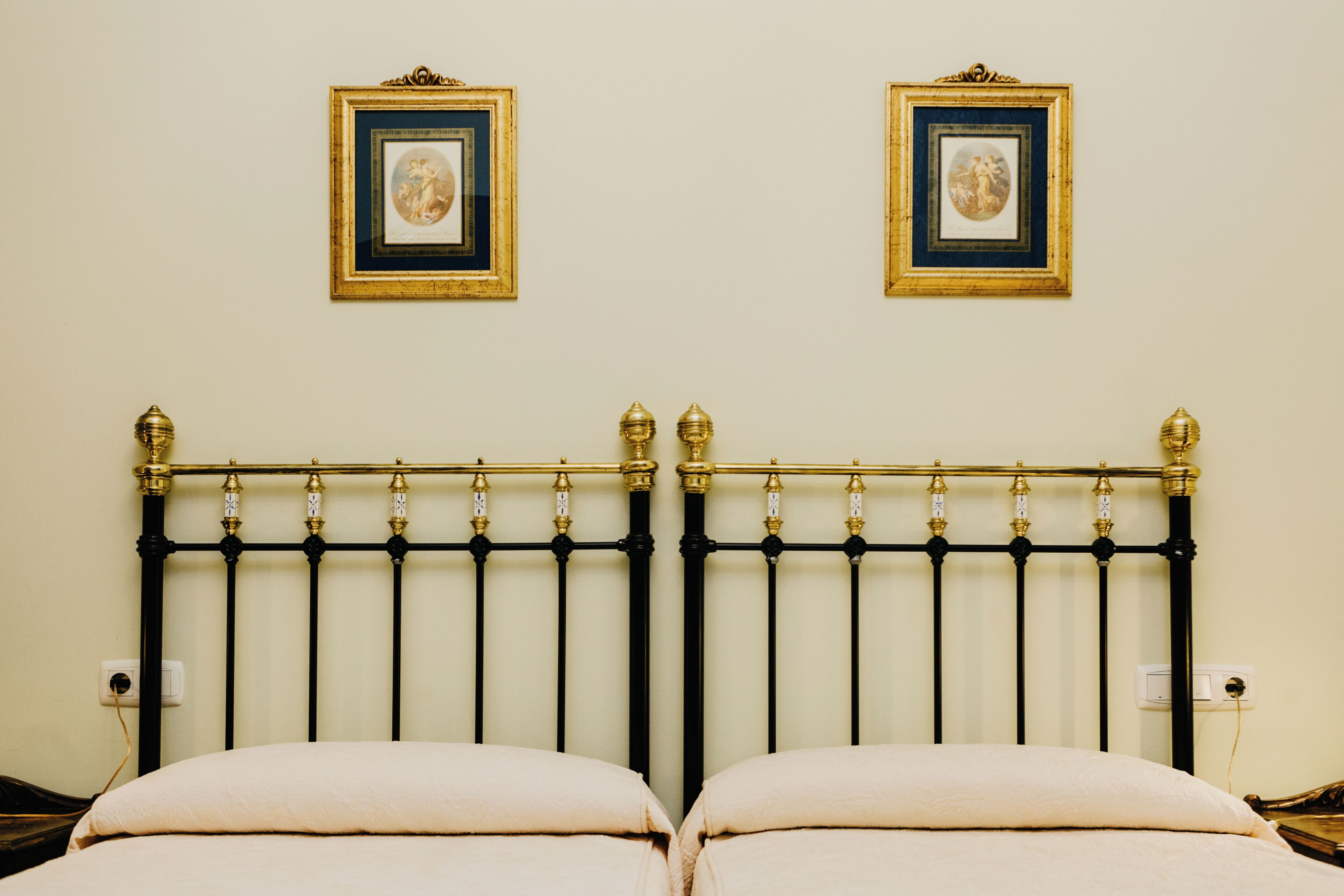 A bed with a black metal headboard, two framed pictures on the wall, and a white wall.