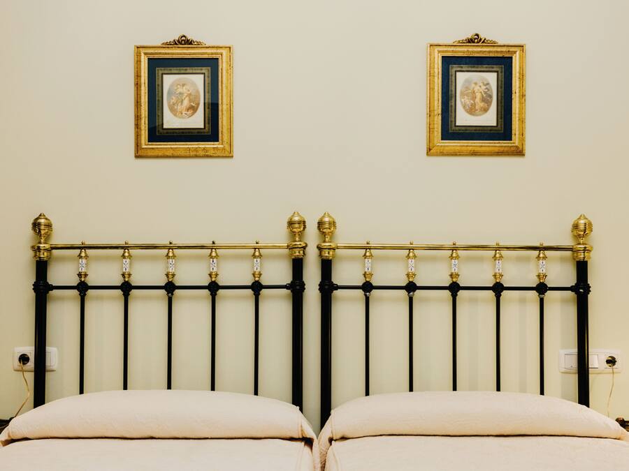 Una cama con cabecera de metal negro, dos cuadros enmarcados en la pared y una pared blanca.