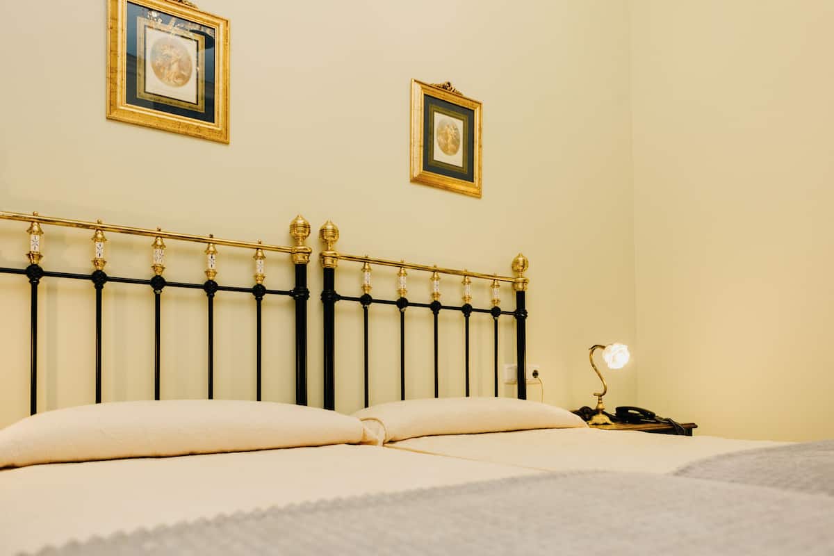 A bed with a black metal headboard, two framed pictures on the wall, and a bedside lamp.