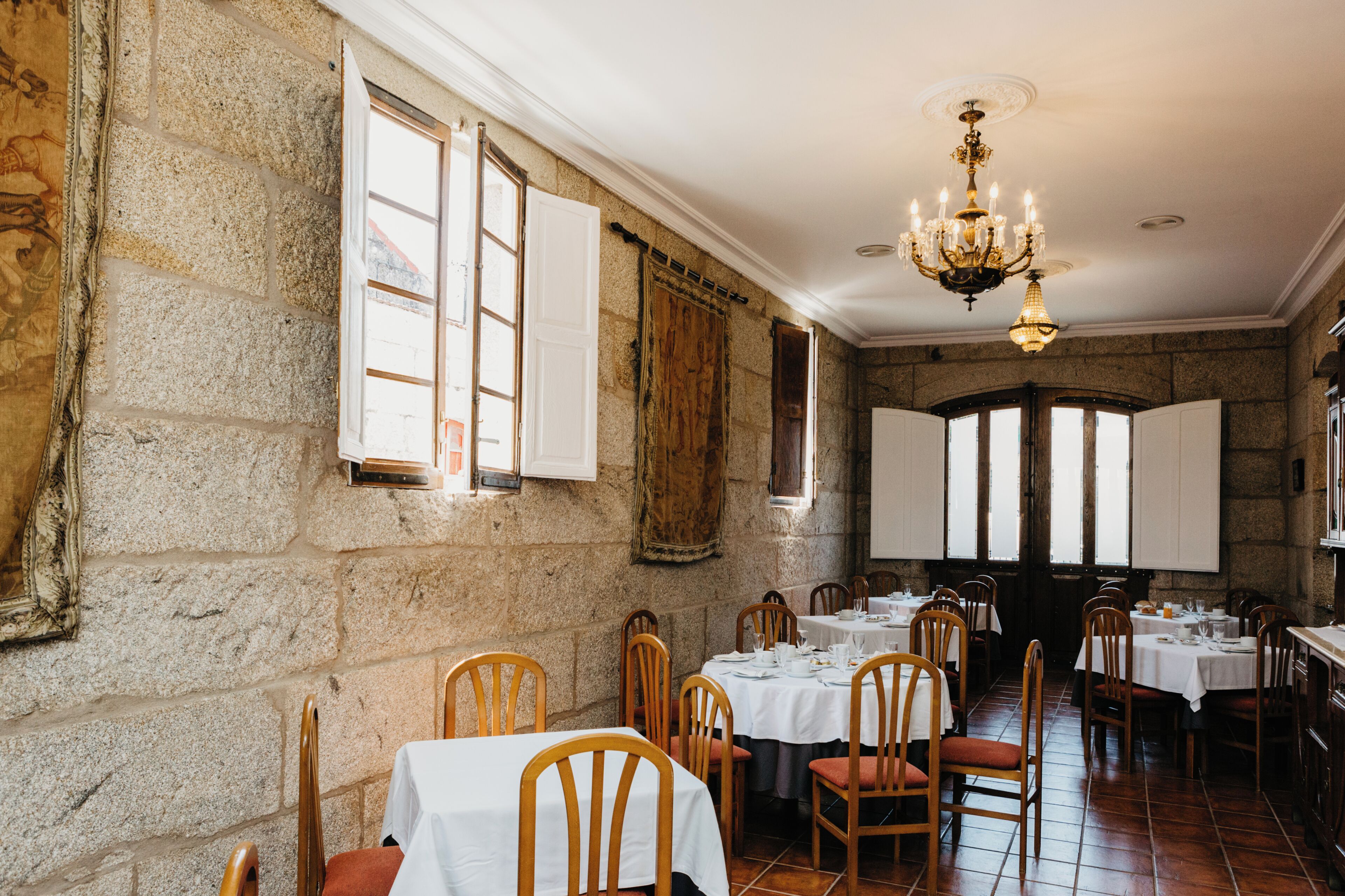 A dining area with stone walls, wooden chairs, and tables set for dining.