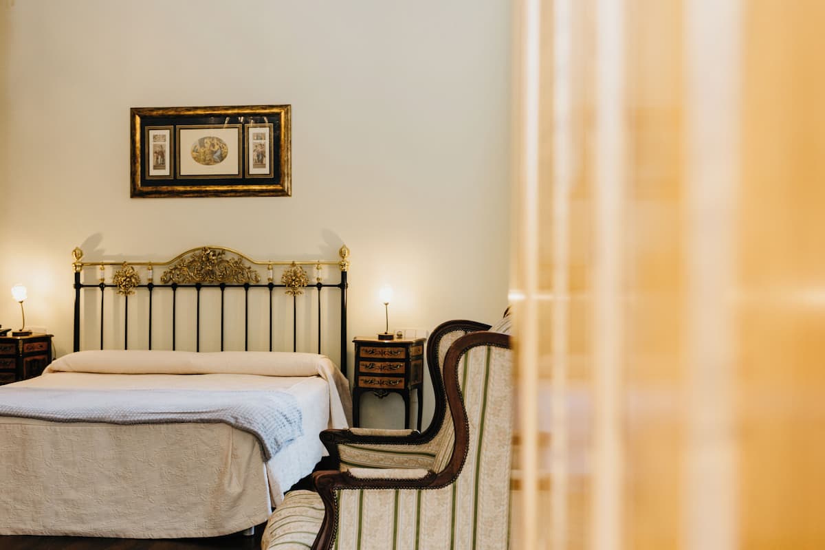 A bedroom with a bed, a chair, a nightstand, and a framed picture on the wall.
