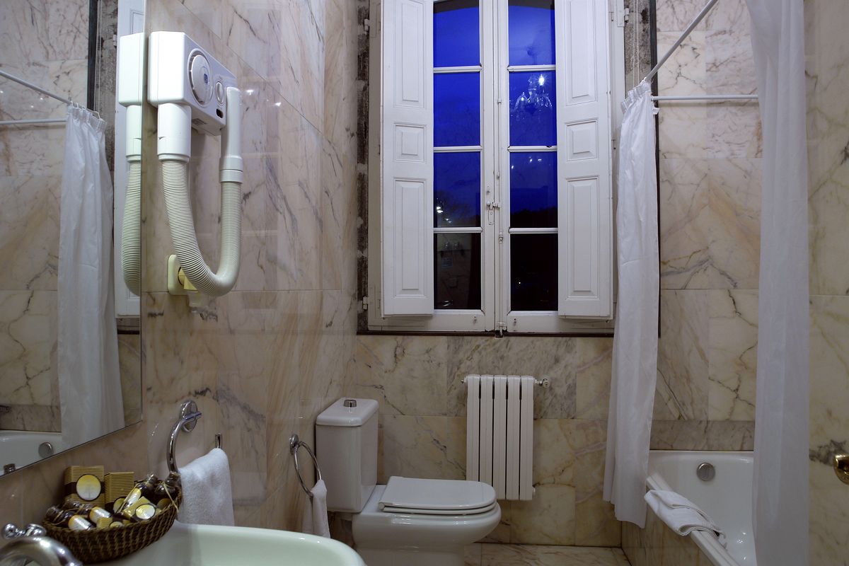 A bathroom with a toilet, bidet, and bathtub. There is a window with curtains, a towel rack, and a radiator.